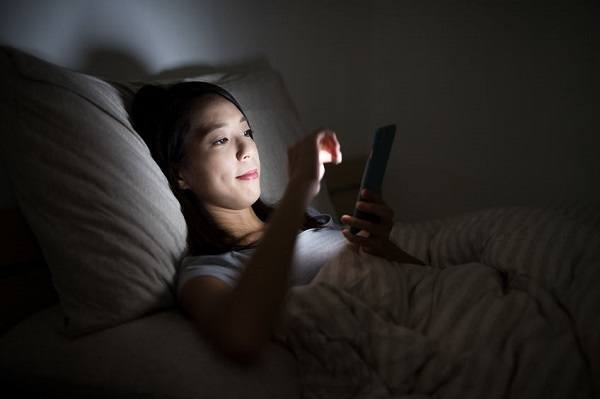 Woman laying in bed, looking at a cell phone at night before going to sleep.