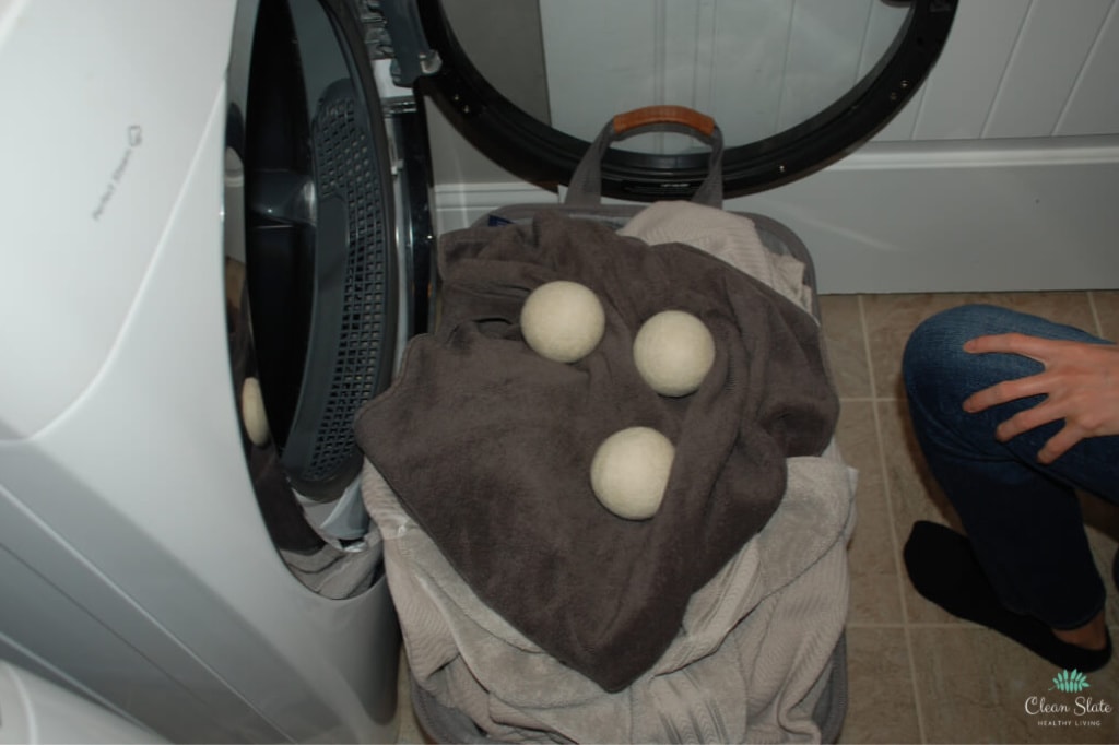 laundry basket filled with laundry and 3 dryer balls. using dryer balls is a great way to speed up drying time