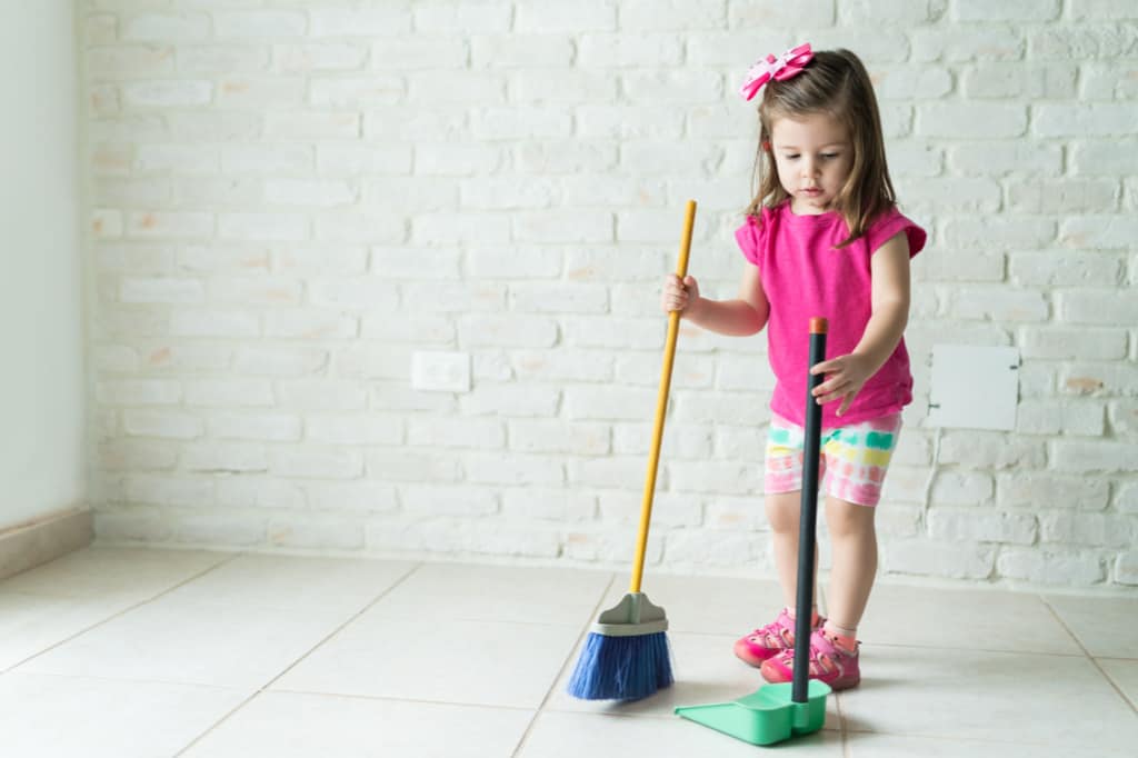 Girl is playing a cleaning game to see how much dirt she can sweep up with her small broom and dust pan