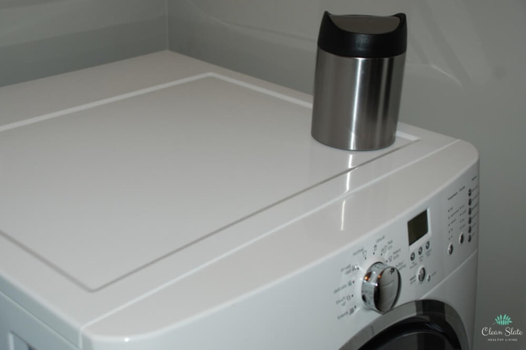 A mini trashcan is sitting on top of the washer in the laundry room. Having a trash can in the laundry room is very useful.