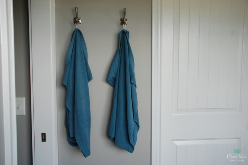 Norwex towels are hanging on hooks in the bathroom. Norwex towels don’t need to be washed as often which saves time on laundry