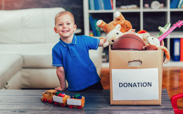 boy sitting next to donation box full of toys that were decluttered from his room