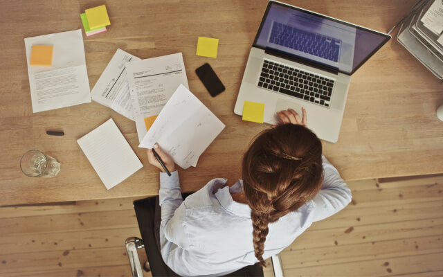 Woman surrounded by papers and working on her computer trying to be productive