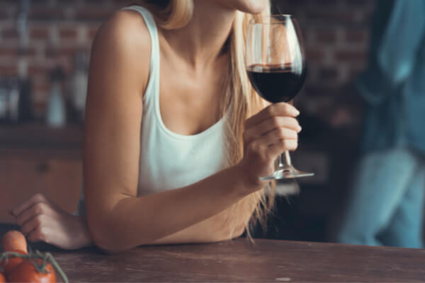 Woman is drinking a glass of red wine. It is important to refrain from drinking alcohol before bed because it disrupts sleep patterns.