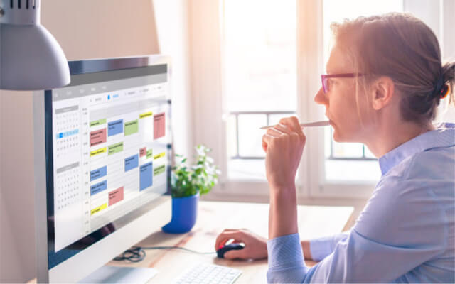 Productive woman sitting at her computer scheduling her to-do list on her digital calendar.