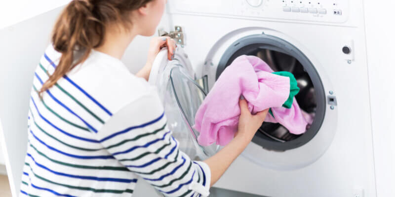 woman is in the laundry room putting clothes in the washer