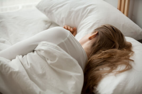 woman trying to get better sleep is sleeping in bed with white sheets