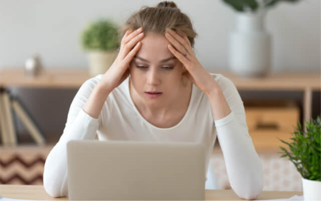 overwhelmed woman has her hands on her head and is looking at her computer
